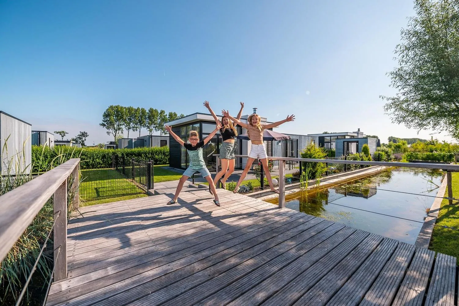Kinder auf Holzsteg vor modernem Ferienpark am Wasser