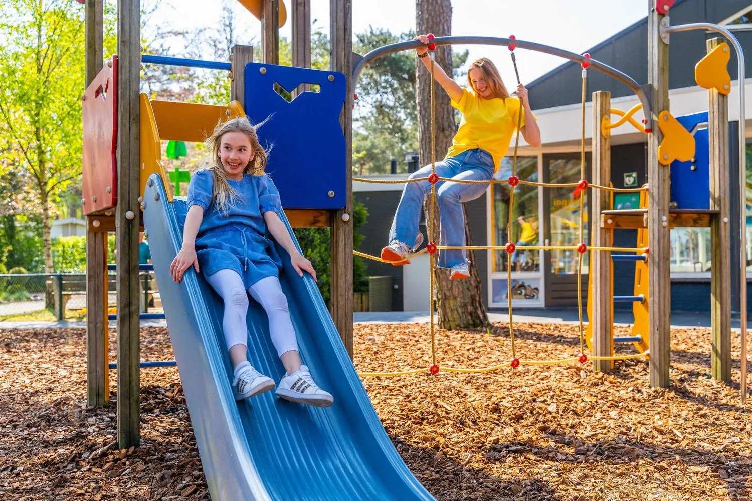 Kinder spielen auf modernem Spielplatz mit Rutsche und Kletterelementen