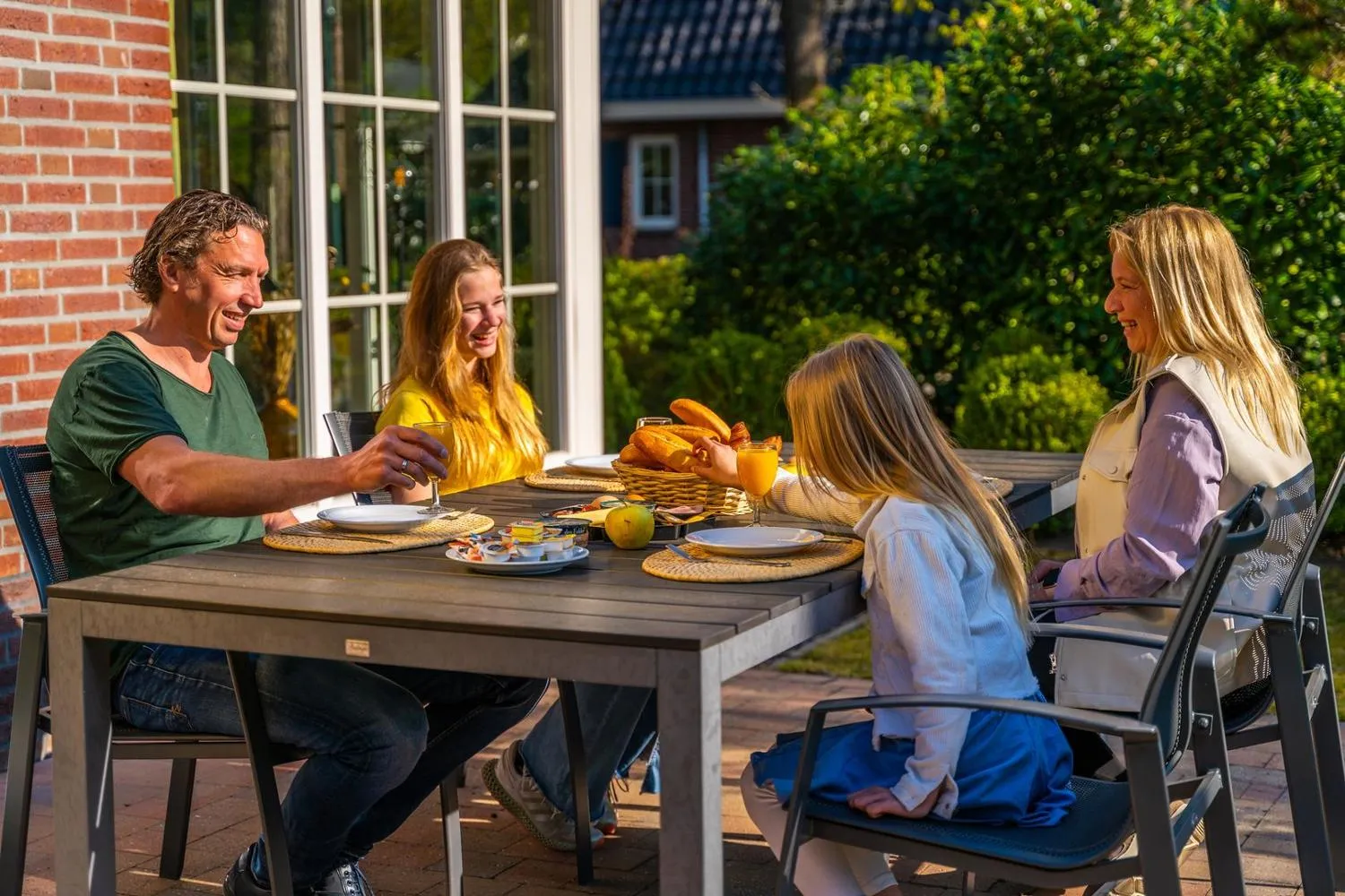 Familie frühstückt auf Terrasse vor Ferienhaus im Park