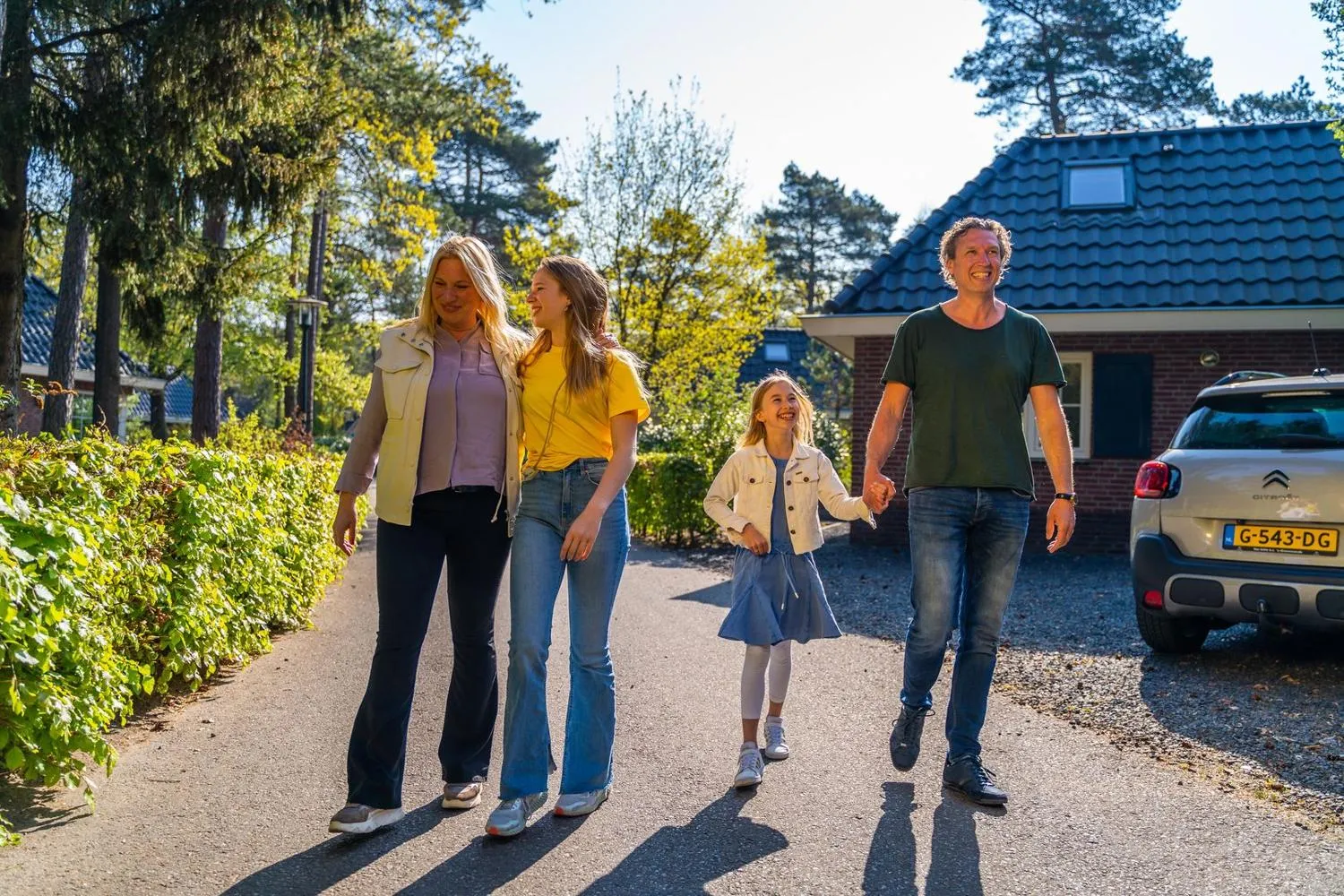 Familie spaziert über Parkweg vor Ferienhaus im Grünen