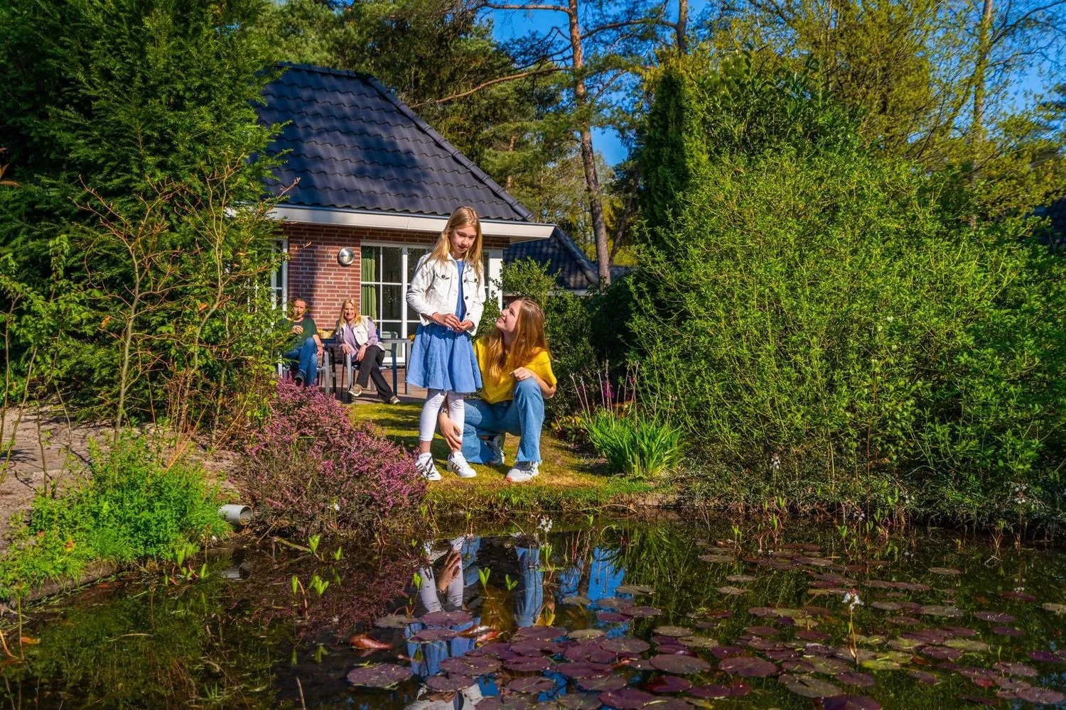 Mutter und Kind vor Ferienhaus neben Gartenteich