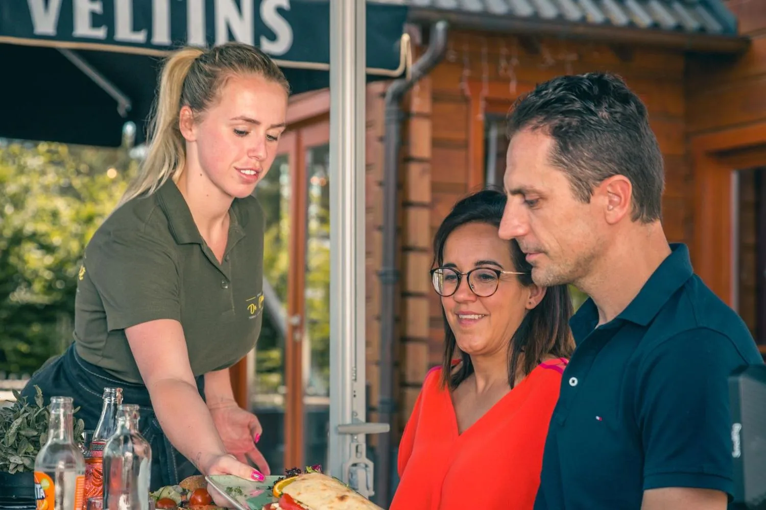 Servicepersonal serviert Gästen auf holzgebauter Parkterrasse