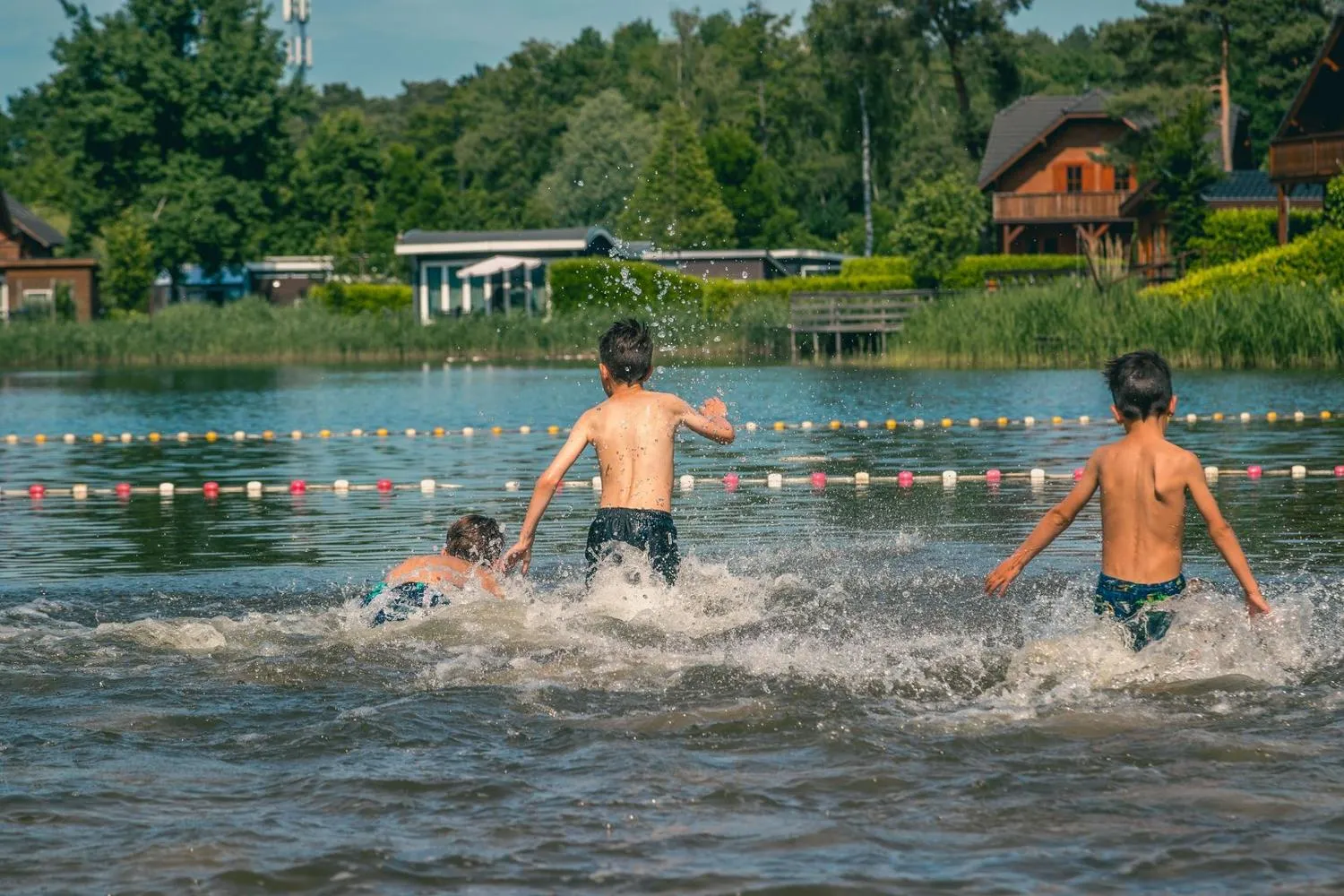 Kinder laufen ins Badewasser, Häuser und Strand dahinter