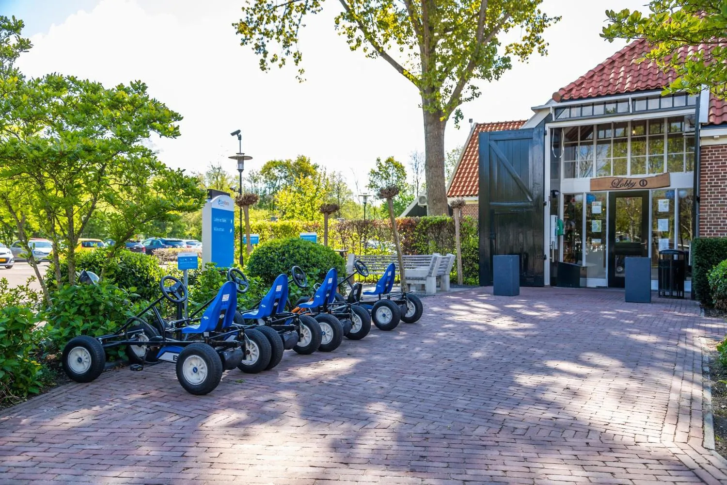 Blaue Tretfahrzeuge zur Ausleihe vor Parkgebäude mit roten Dachziegeln