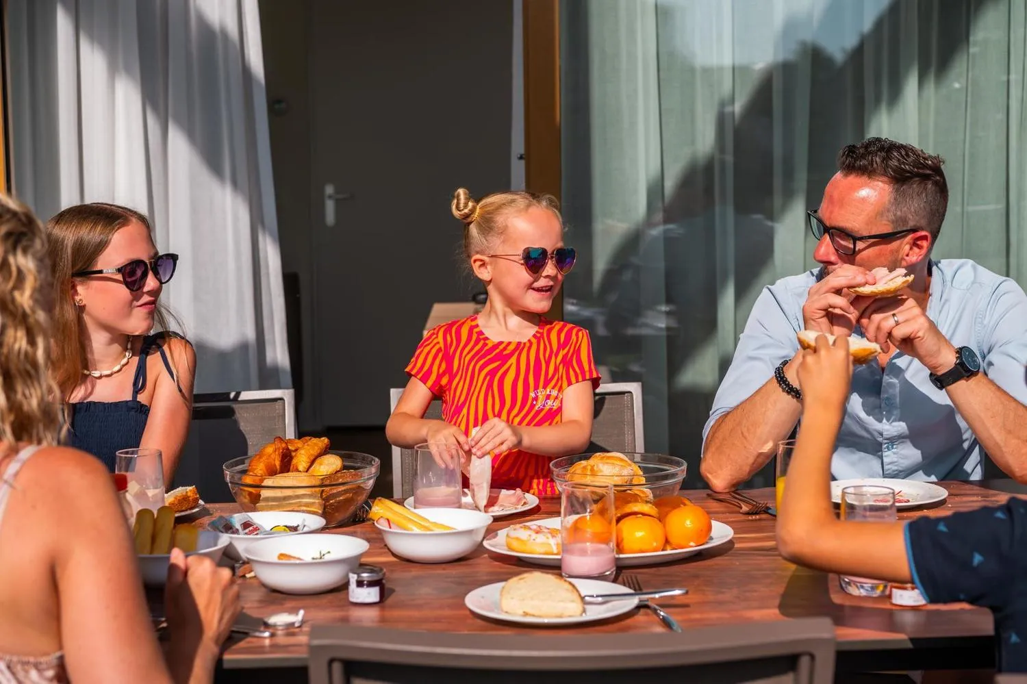 Familie beim Brunch an Tisch vor modernem Ferienhaus