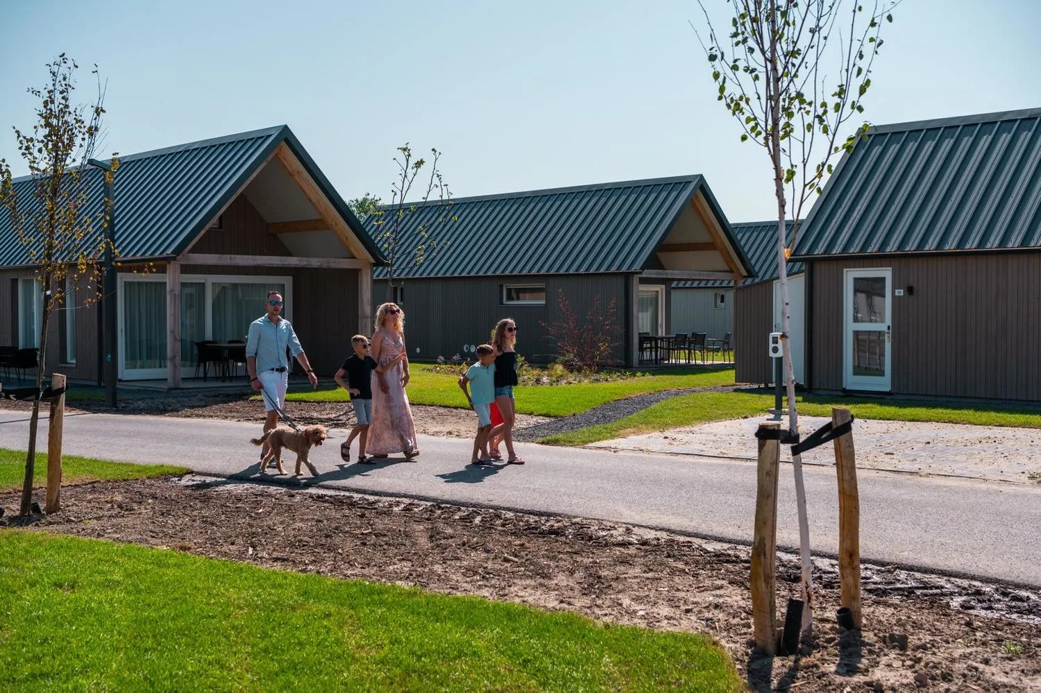 Familie mit Hund spaziert zwischen modernen Ferienhäusern