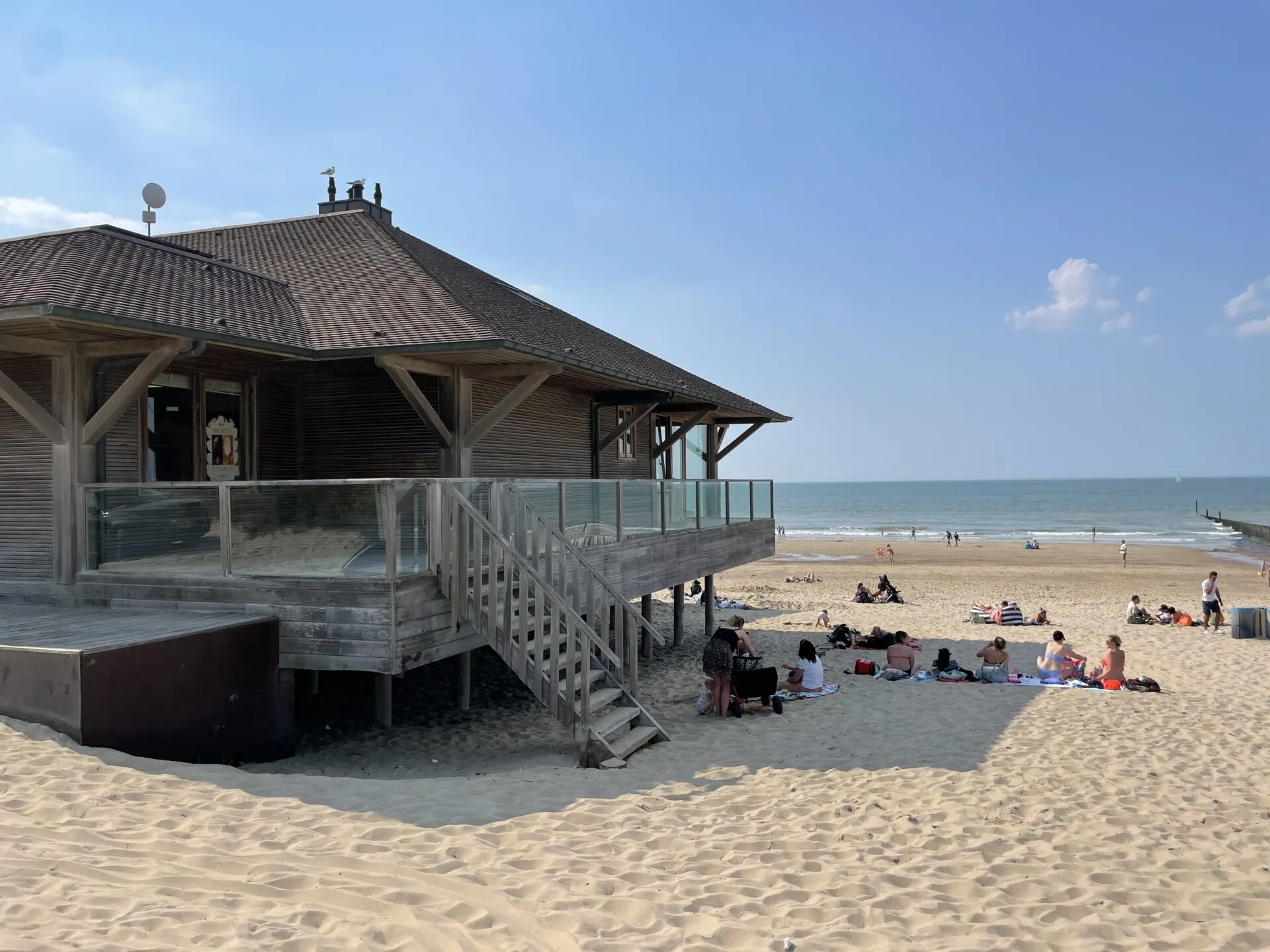 Strandpavillon mit Terrasse, Sandstrand mit Besuchern und Meer