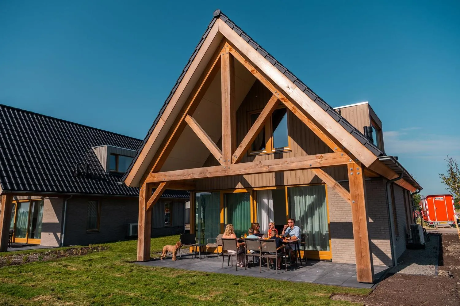 Familie unter Holz-Veranda vor modernem Ferienhaus mit Terrasse
