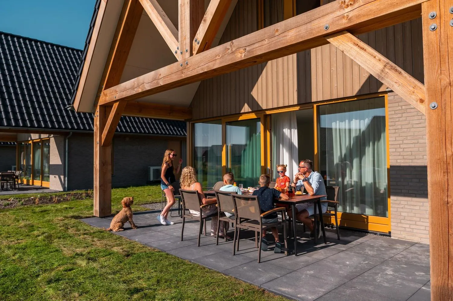 Familie beim Essen an Tisch unter Holzveranda mit Dach