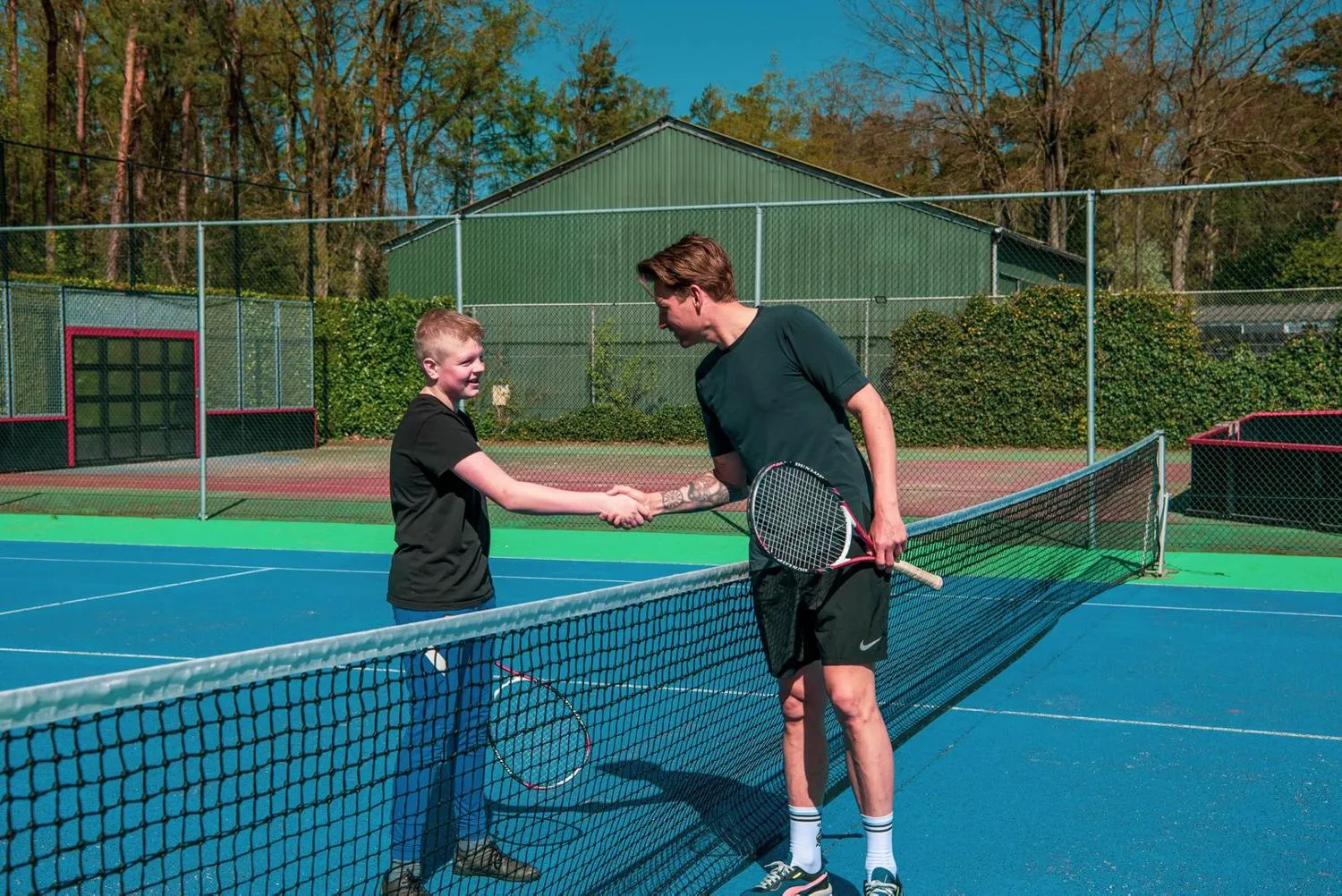 Tennisplätze mit blau-grüner Oberfläche im von Wald umgebenen Ferienpark