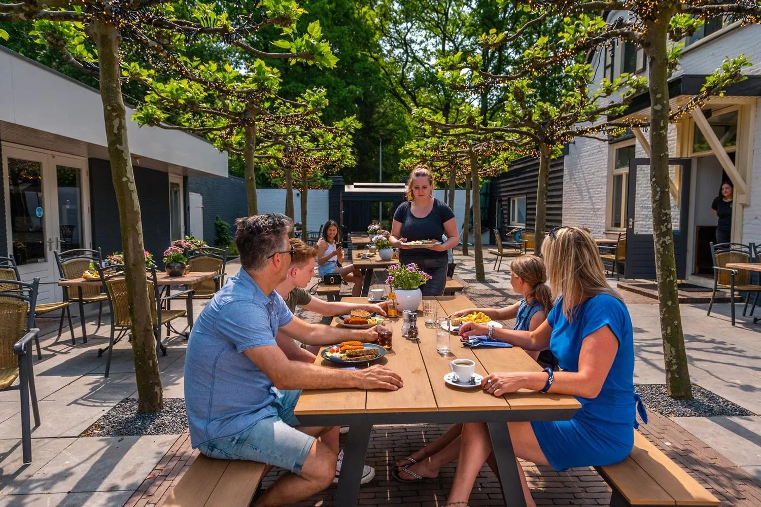 Restaurant-Außenbereich mit Pergola und Picknick-Tischen, moderne Häuser dahinter