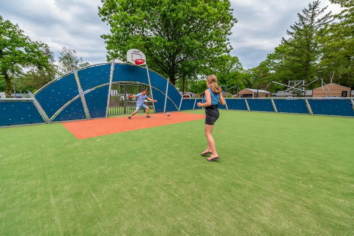 Überdachte Multisportanlage mit blauem Dach auf großem grünem Rasenplatz