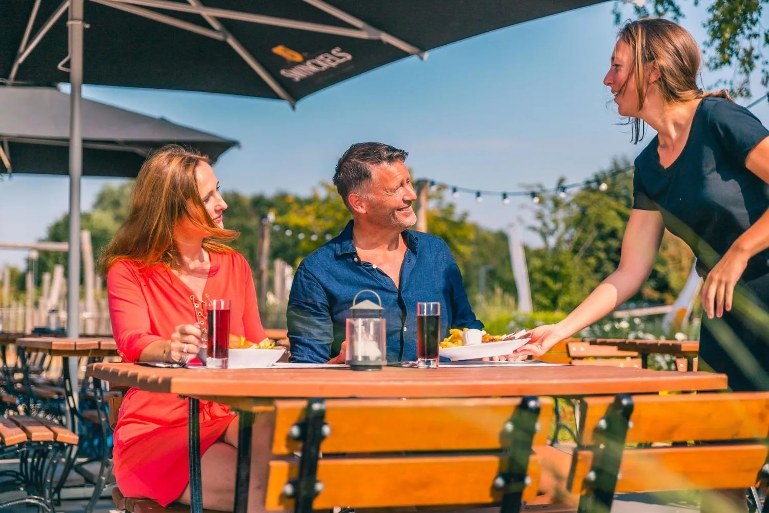 Gäste genießen Mahlzeit unter Schattendach auf einer Terrasse