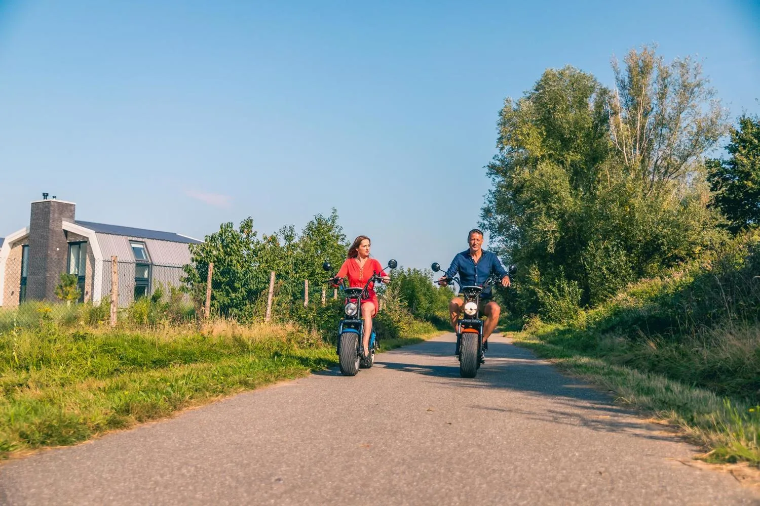 Paar fährt mit Rollern durch den Parkweg zwischen Unterkünften