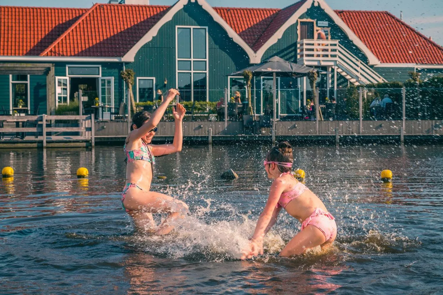 Mädchen spielen im Wasser vor grünen Häusern mit roten Dächern