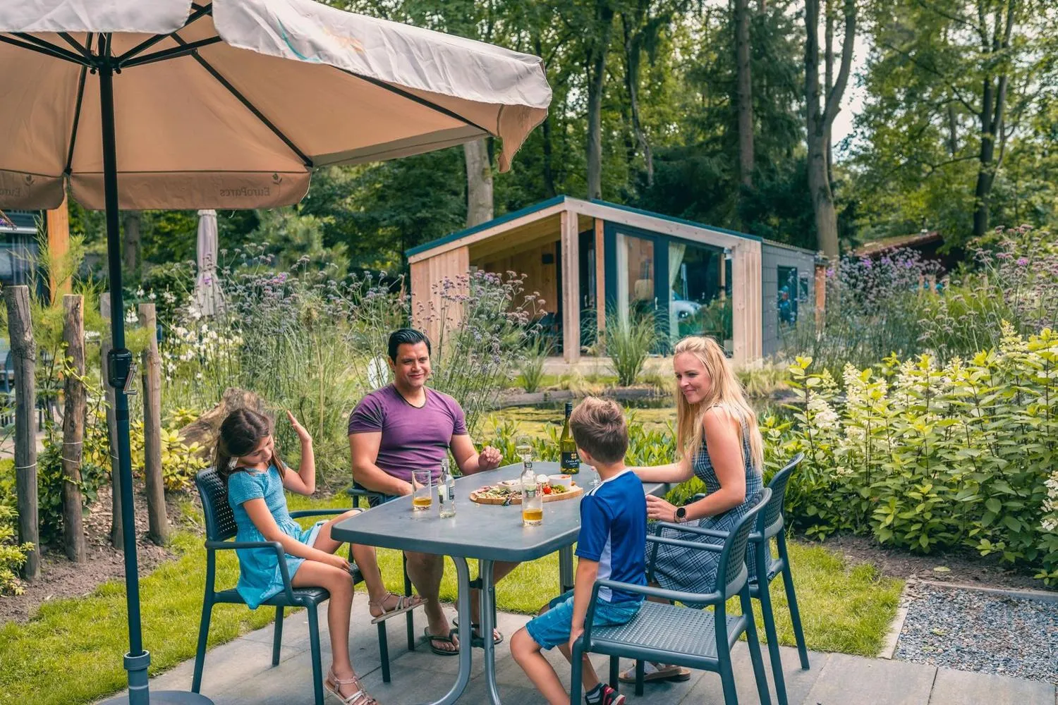 Familie isst unter Sonnenschirm im blühenden Gartenbereich