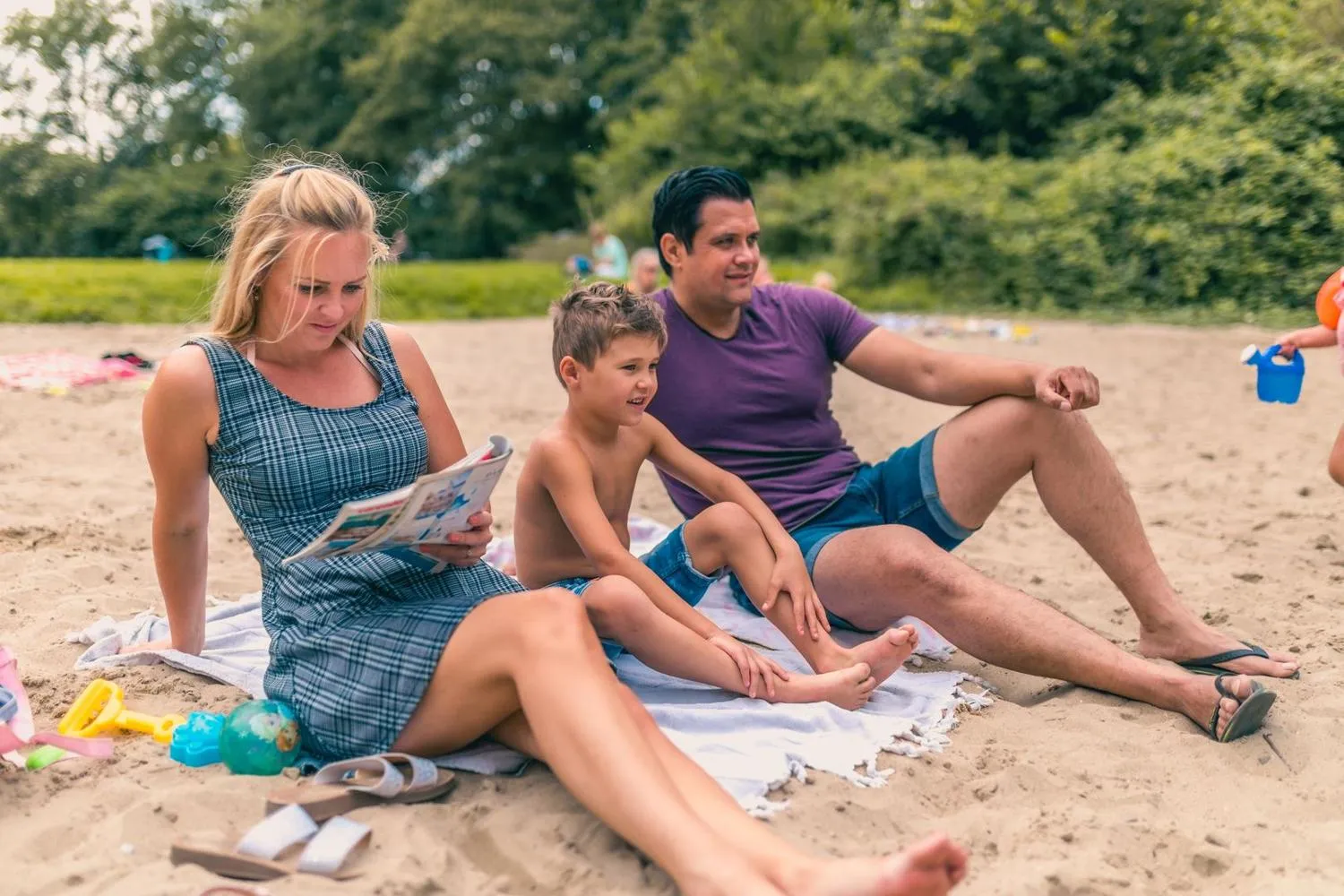 Familie sitzt am Sandstrand und liest Zeitung gemeinsam
