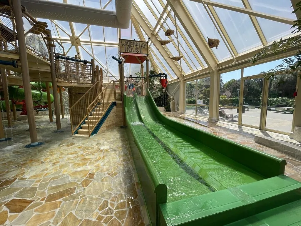 Wasserspielplatz mit grünen Wasserrinnen und Spielgeräten unter Glaskuppel