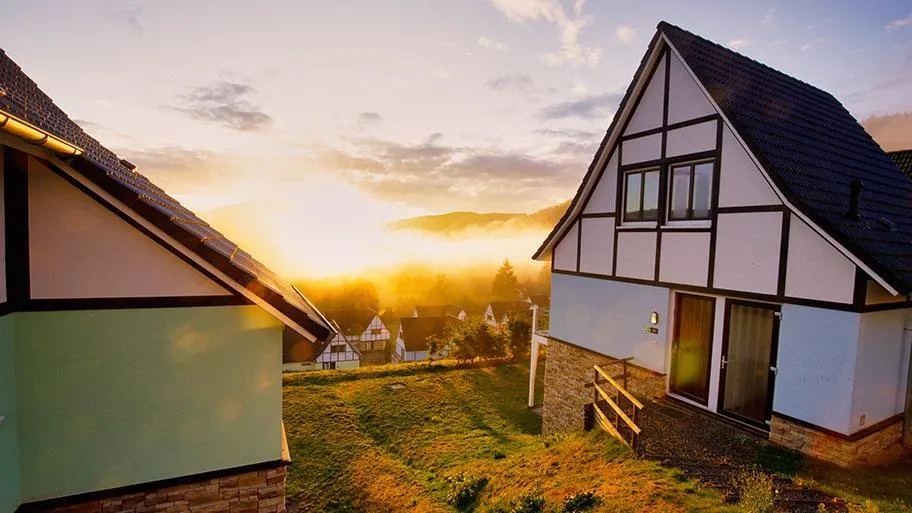 Fachwerkgebäude mit goldenem Sonnenuntergang und waldiger Naturlandschaft