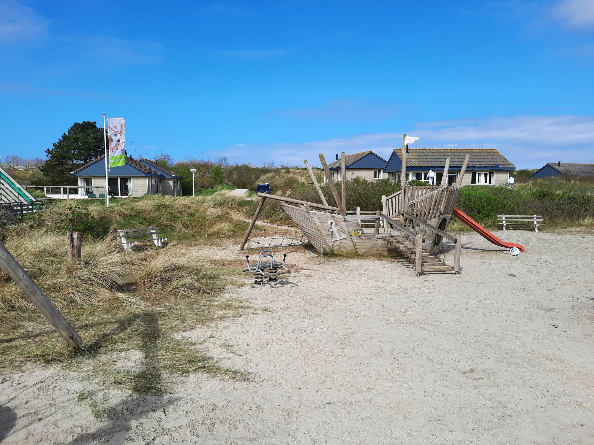 Ferienhäuser hinter den Dünen auf Texel, davor ein Sandspielplatz mit Piratenschiff